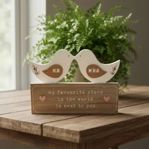 Wooden mantel plaque featuring two white kissing birds labelled “Mr” and “Mrs”, with pink hearts and the message “My favourite place in the world is next to you.”