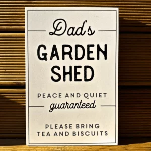 Cream rectangular wooden sign reading “Dad’s Garden Shed – Peace and Quiet Guaranteed. Please Bring Tea and Biscuits”, displayed against a wooden background.