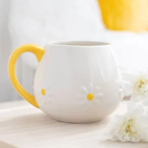 White ceramic mug with embossed daisy design and yellow handle on a light wooden surface.