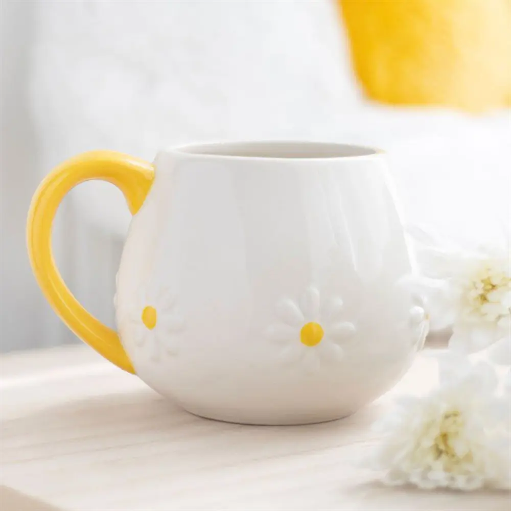 White ceramic mug with embossed daisy design and yellow handle on a light wooden surface.