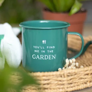 Green enamel mug with white quote “You’ll find me in the garden”, styled in a wicker basket beside gardening tools and plants.
