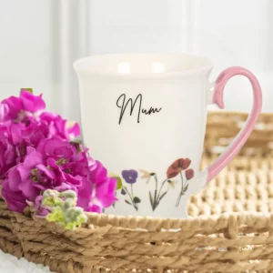 Mum wildflower mug with pink handle displayed in wicker basket beside bright pink flowers.