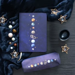 Solar system stationery bundle featuring an A5 notebook with gold-edged pages and a matching navy pencil case on a dark background